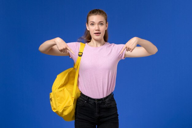 Вид спереди молодой женщины в розовой футболке, носить желтый рюкзак позирует