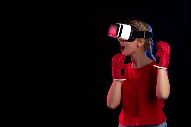 Front view of young female playing vr in mma gloves on a dark wall