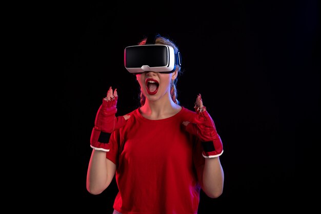 Front view of young female playing vr in mma gloves on dark wall