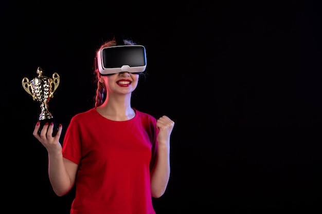 Front view of young female playing vr with winner cup on a dark wall