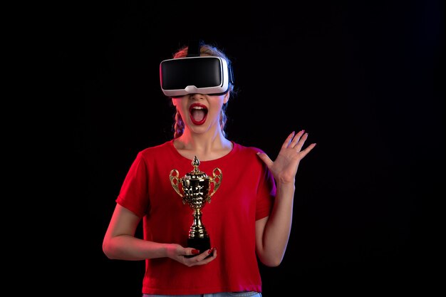 Front view of young female playing vr with winner cup on a dark wall