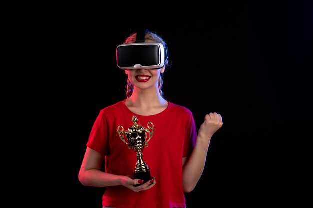 Front view of young female playing vr with winner cup on the dark wall