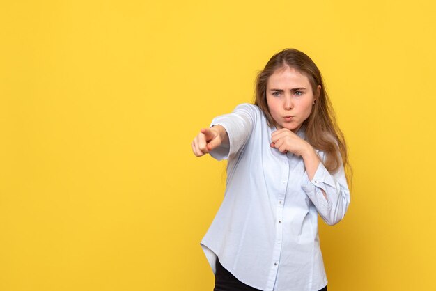 Front view of young female pointing on yellow wall