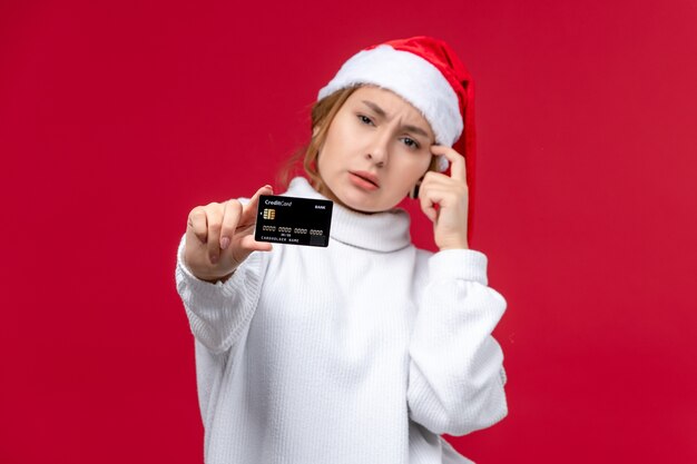 Вид спереди молодая женщина позирует с банковской картой на красном фоне