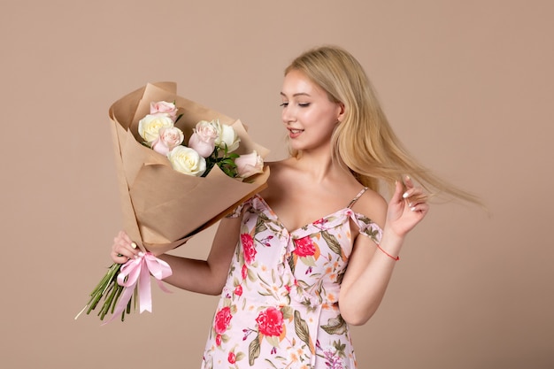 Front view of young female posing with bouquet of beautiful roses on brown wall