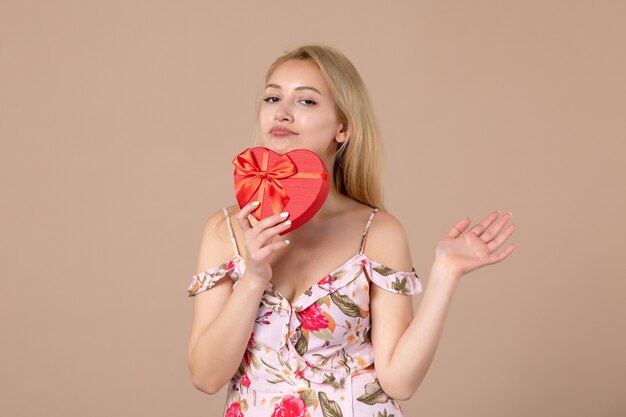 Front view of young female posing with red heart shaped present on brown wall