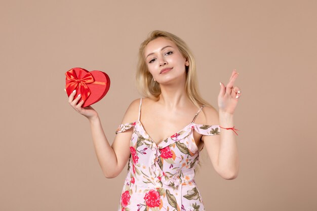 Front view of young female posing with red heart shaped present on brown wall