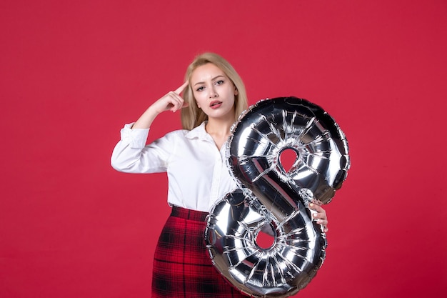 Free photo front view young female posing with silver balloon as march symbol on red background equality femininity womens day color sensual feminine affectionate