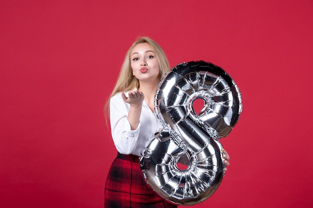 Front view young female posing with silver balloon as march symbol on red background sensual feminine femininity affectionate womens day equality color