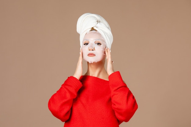 Vista frontale giovane femmina si prepara ad applicare la maschera per il viso su sfondo rosa