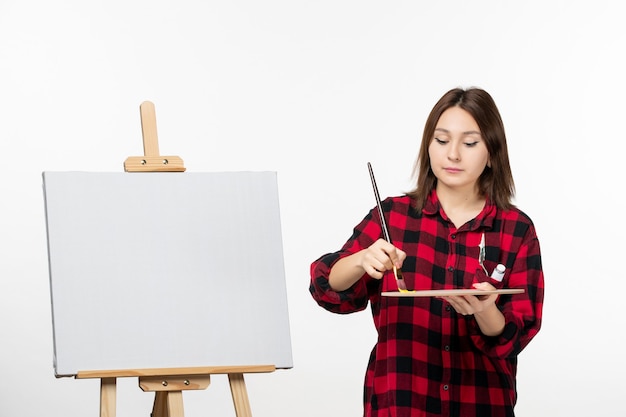 Front view young female preparing to paint on easel on white wall