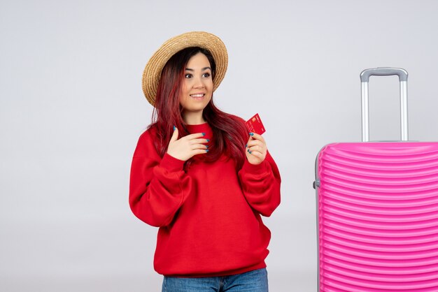 Вид спереди молодая женщина готовится к поездке и держит банковскую карту на белой стене, отпускные цветные полеты, летнее путешествие эмоций