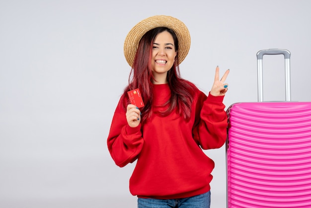 Front view young female preparing for trip and holding bank card on white wall