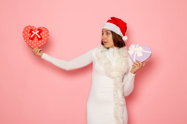 Free photo front view of young female in red cap holding heart shaped presents on a pink wall