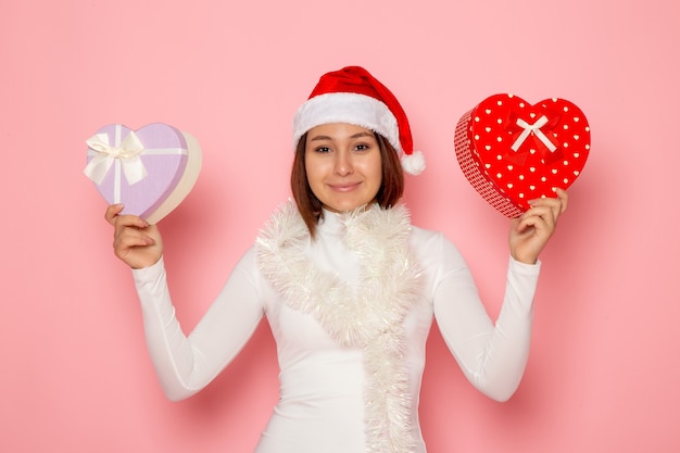 Front view of young female in red cap holding heart shaped presents on pink wall