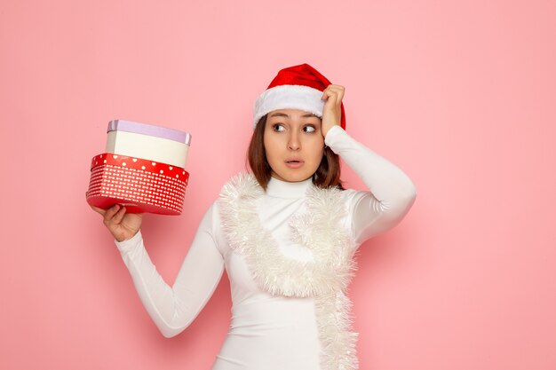 Front view of young female in red cap holding heart shaped presents on pink wall