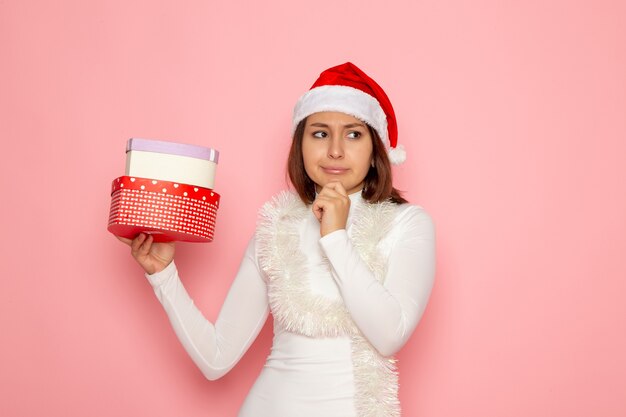 Front view of young female in red cap holding heart shaped presents thinking on pink wall