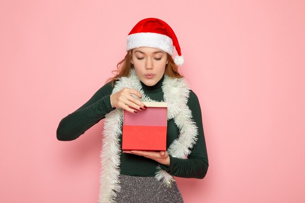 Front view of young female in red cap holding present on pink wall
