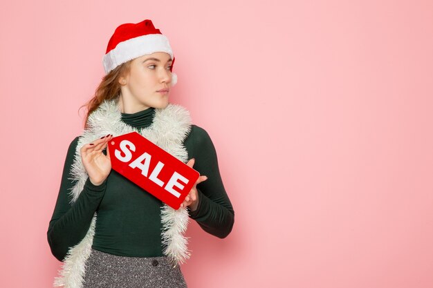 Front view of young female in red cap holding sale writing on pink wall