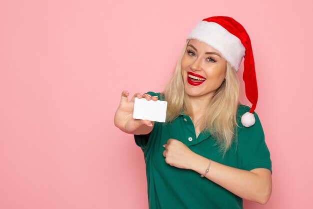 Front view of young female in red cap holding white card on pink wall