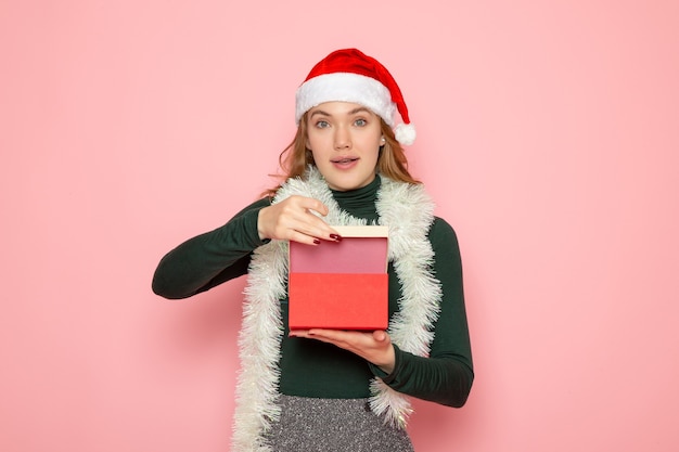 Front view of young female in red cap opening present on pink wall