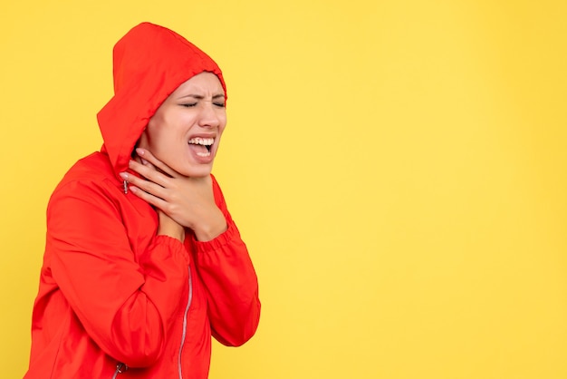 黄色の背景に喉の痛みを持っている赤いコートの若い女性の正面図