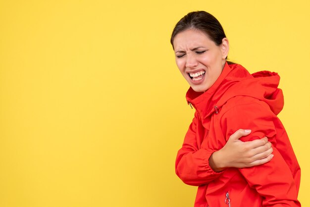 Front view young female in red coat with hurt arm on yellow background