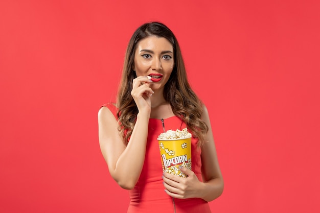 Front view young female in red shirt eating popcorn watching movie on red surface