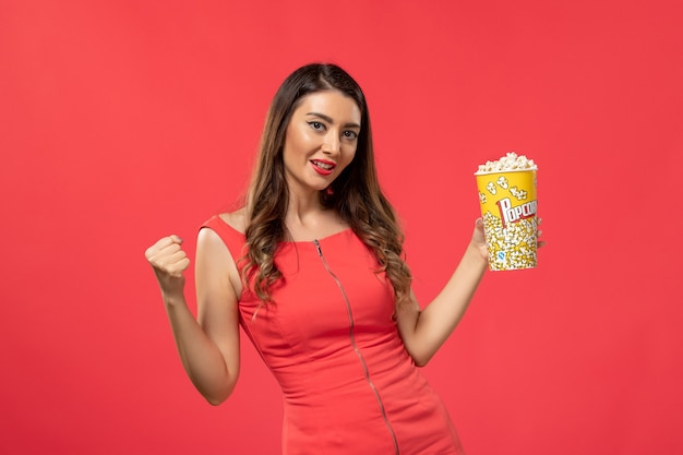 Front view young female in red shirt holding popcorn on light red surface