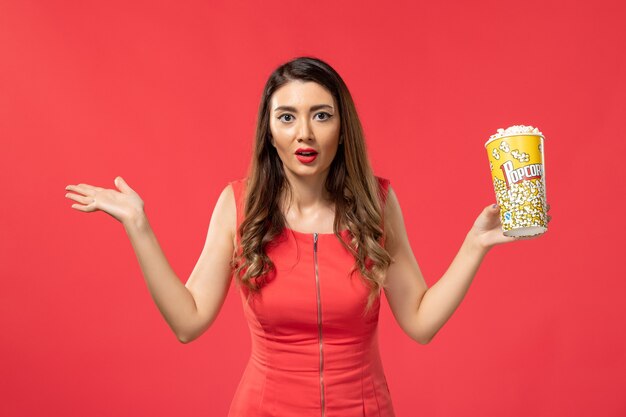 Front view young female in red shirt holding popcorn package on red surface