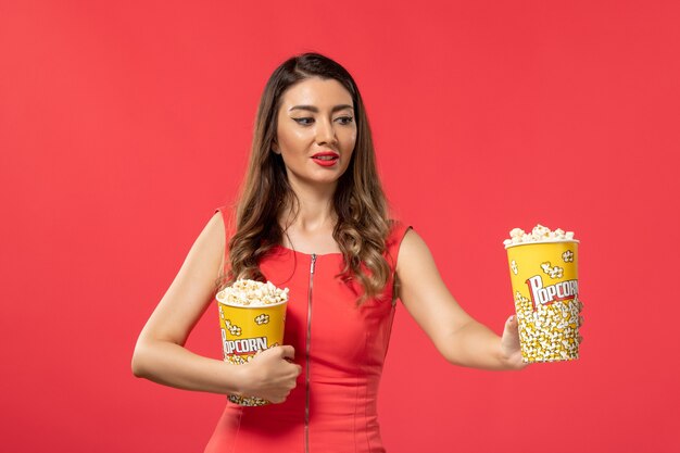 Front view young female in red shirt holding popcorn packages on red surface