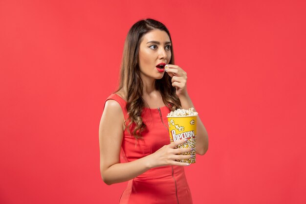 Front view young female in red shirt holding popcorn on red desk