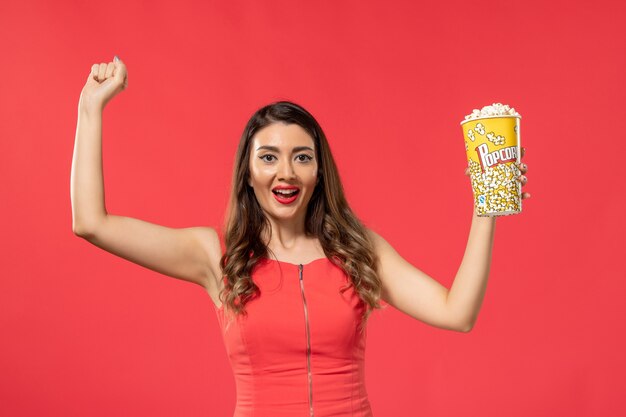 Front view young female in red shirt holding popcorn and rejoicing on red surface