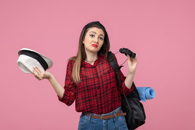 Front view young female in red shirt using binoculars on the pink background color woman human