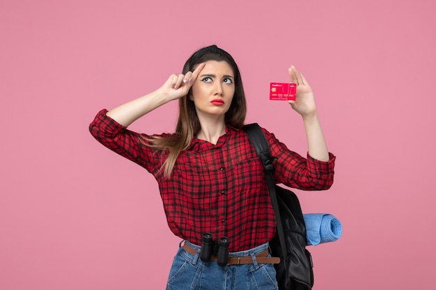 Вид спереди молодая женщина в красной рубашке с банковской картой на розовом фоне цвета человеческой женщины