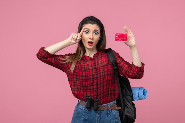Вид спереди молодая женщина в красной рубашке с банковской картой на розовом фоне цвета человеческой женщины