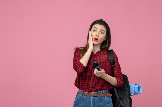 Front view young female in red shirt with binoculars on the pink background color human woman