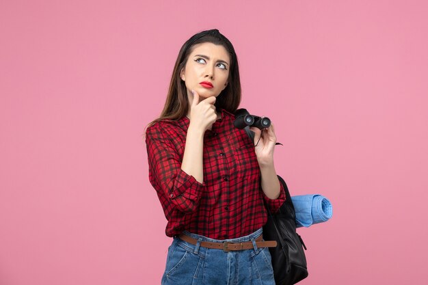 Front view young female in red shirt with binoculars on a pink background color woman student