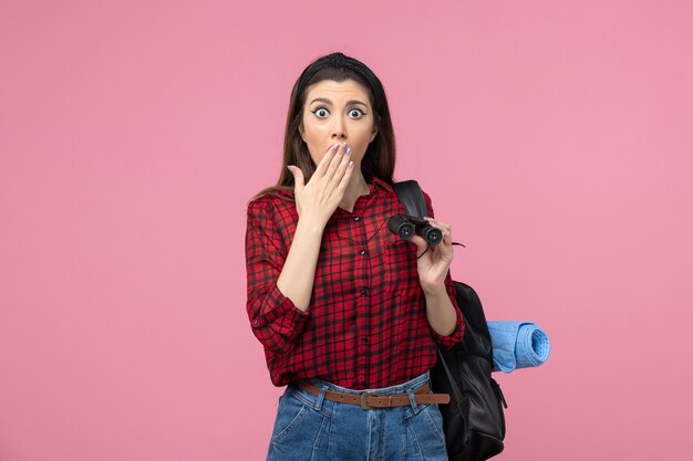 Front view young female in red shirt with binoculars on a pink background student color woman