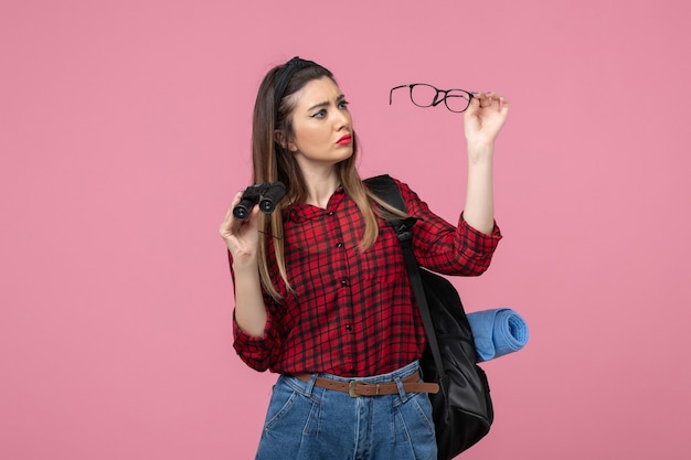 ピンクの背景の女性の写真モデルに双眼鏡で赤いシャツを着た若い女性の正面図