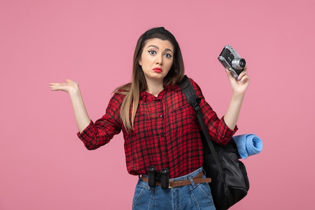 ピンクの背景の写真の女性モデルにカメラと赤いシャツを着た若い女性の正面図