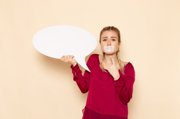 Free photo front view young female in red shirt with tied mouth and holding white sign on the cream space female cloth  photo violence domestic