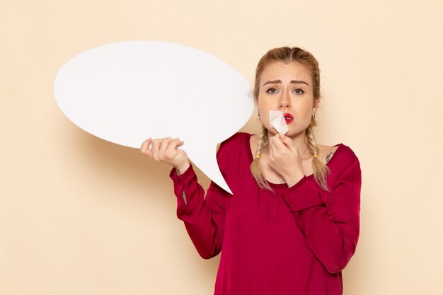 Front view young female in red shirt with tied mouth holding white sign on the cream space female cloth  photo violence domestic