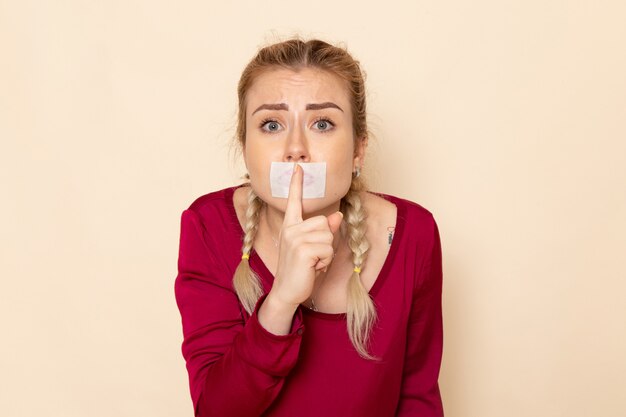 クリームスペースの女性布写真に沈黙の兆しを見せ結ばれた口のある赤いシャツの正面の若い女性