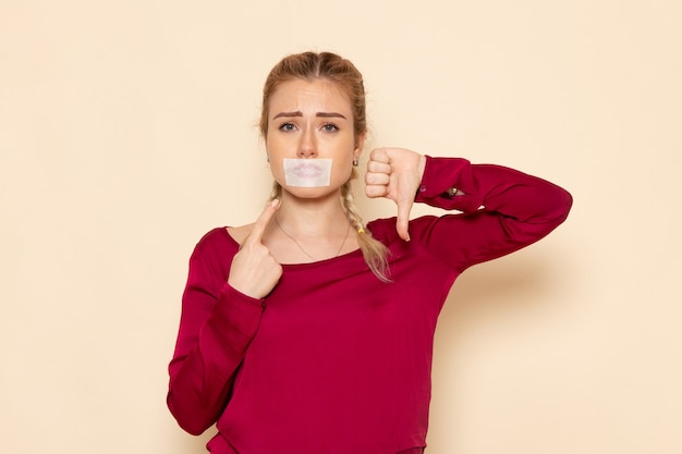 Front view young female in red shirt with tied mouth showing unlike sign on the cream space female cloth  photo violence domestic