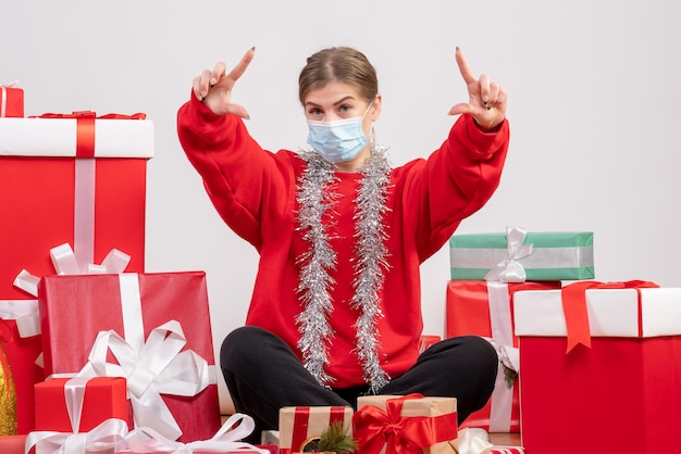 Front view young female sitting around christmas presents in mask