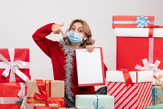 Front view young female sitting around christmas presents in mask