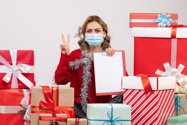 Front view young female sitting around christmas presents in mask