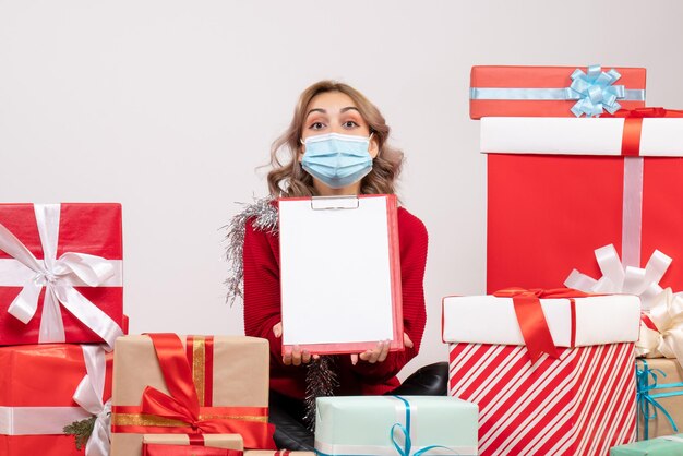 Front view young female sitting around christmas presents in mask