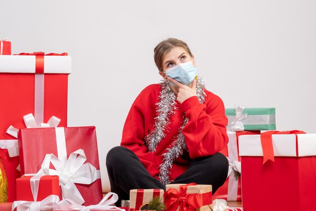 Front view young female sitting around christmas presents in mask